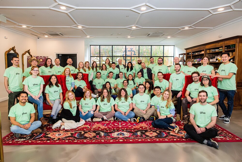 A group photo of all the Glue employees (about 50 people), all wearing a bright mint-colored tee-shirt, in the lobby of an hotel.
